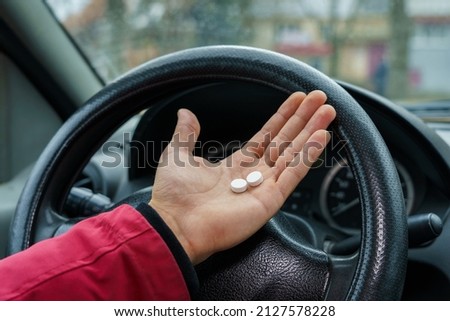 Two pills in the hand or on the palm of the driver against a blurred background of the steering wheel in the car. The use of pharmacological drugs for medical purposes while driving. Selective focus