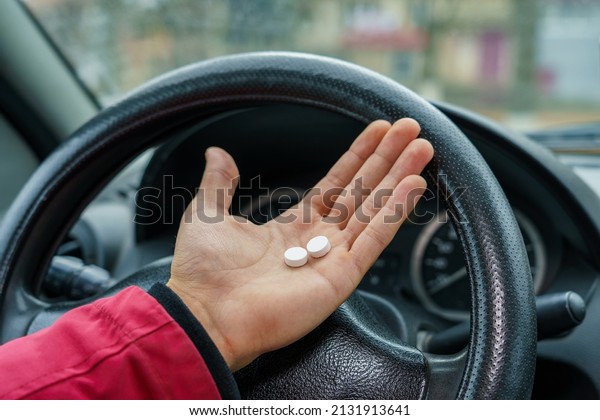 Two pills in the hand or on the palm of the driver
against a blurred background of the steering wheel in the car. The
use of pharmacological drugs for medical purposes while driving.
Selective focus