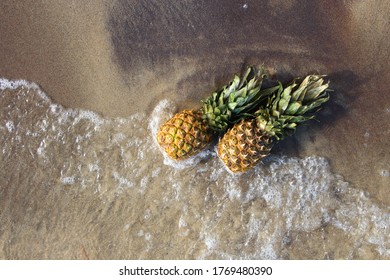 two pineapples in the waves on the beach. A pineapple on the beach.