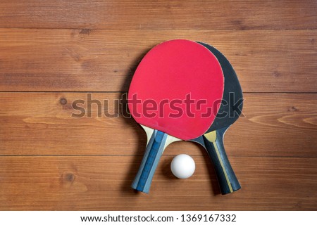 Two ping-pong rackets and a ball on a brown wooden background, close-up.