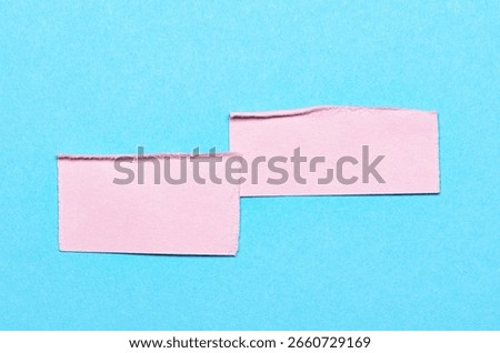 Two pink overlapping torn ripped blank paper notes with folded edge dog-ear earmark and copy space for text on blue background