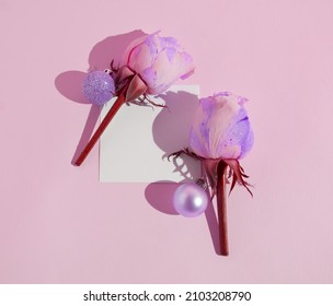 Two pink and purple roses with shiny pink baubles with a note on a pink background. Minimalist concept of love and affection. Valentine’s or anniversary concept. Floral pattern. Copy space. Flat lay.