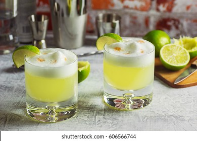 Two Pisco Sour Cocktails With Ingredients And Bottles On A Bar