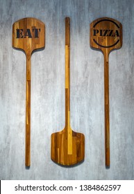 Two pizza paddle with text "eat" and "pizza" hang on concrete wall for background