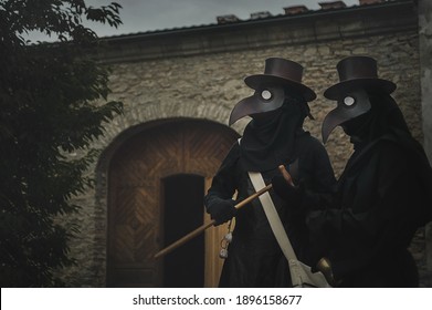 Two Plague Doctors In Masks On Medieval Castle Background. Reconstruction Of Medicine Costumes. Mascarade Historical Costumes And Mask 