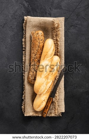 Two plain baguettes and one seeded loaf arranged on burlap cloth with a rustic bread knife on a dark stone surface