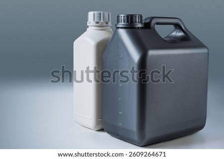 Two plastic containers, one white and one black, made of HDPE, stand side by side on a neutral background, used for storing liquids or chemicals.