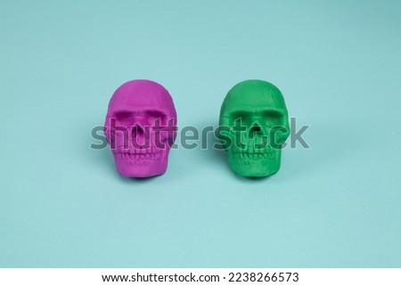 Two plastic skulls, one pink and one green, placed on a turquoise background. Minimal and creative color still life photography 