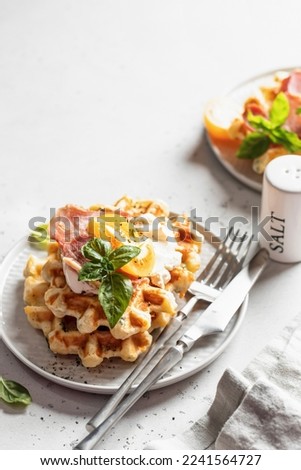 Two plates of cheese or potato savory waffles served with tomatoes, cream cheese, ham and bazil leaves with cutlery and linen napkin. Delisious savory breakfast. Vertical orientation