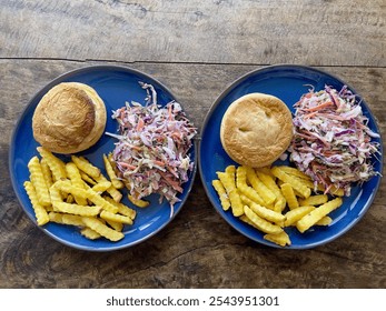 Two plates of savoury pie and french fries with coleslaw on a rustic wooden table - Powered by Shutterstock