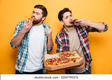 Two pleased men in shirt eating pizza and looking at the camera over yellow background