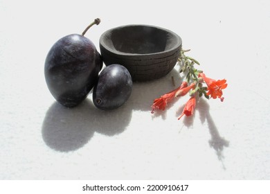 Two Plums, A Cup And Small Orange Flowers.