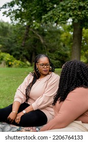 Two Plus Size Black Friends Sitting Down Hanging Out At The Park