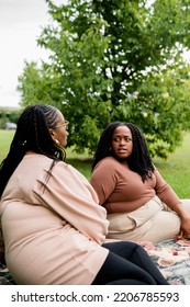 Two Plus Size Black Friends Sitting Down Hanging Out At The Park