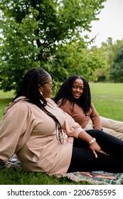 Two Plus Size Black Friends Sitting Down Hanging Out At The Park