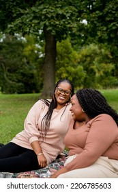 Two Plus Size Black Friends Sitting Down Hanging Out At The Park