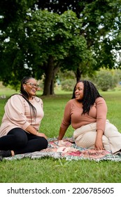 Two Plus Size Black Friends Sitting Down Hanging Out At The Park