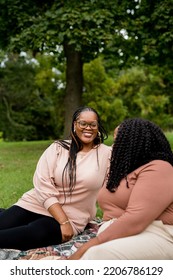 Two Plus Size Black Friends Sitting Down Hanging Out At The Park