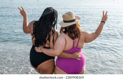 Two plus size models pose making the peace sign with their fingers. Couple of girls enjoy a day at the beach. Two young women on vacation at the beach.