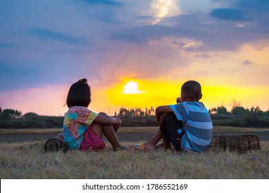 Two poor children sit on the field and look at the sunset. poor asian student playing on the field