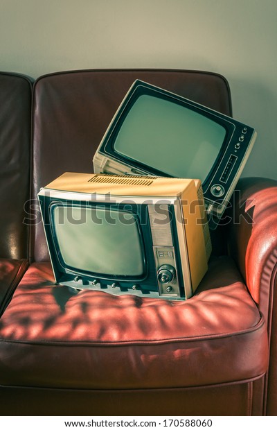 Two portable\
vintage televisions on red\
couch