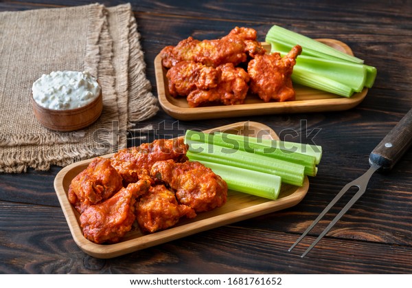 Two portions of buffalo wings with fresh celery\
stalks and blue cheese dip