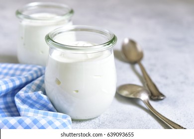 Two portions of fresh natural  homemade organic yogurt in a glass jar on a light slate background.