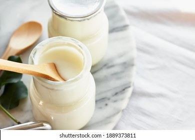 Two portions of fresh natural organic yogurt in a glass jars on marble tray. Homemade greek yogurt with wooden spoons. Healthy breakfast. Top view.