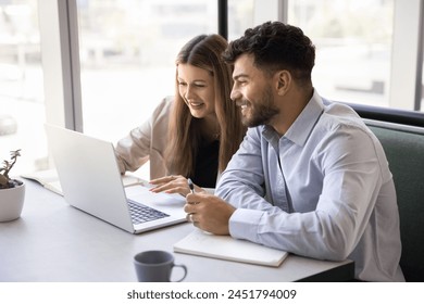 Two positive colleagues working on project at laptop in coworking cafe, typing, talking on video call, smiling, discussing cooperation strategy, enjoying communication communication - Powered by Shutterstock