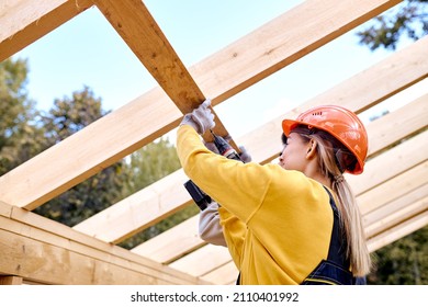 Two Positive Contractors Working With Drill Driver. Carpenter Working on Wooden House Skeleton Frame Roof Section. Construction Industry Theme. Woman In Hardhat Is Laughing During Work - Shutterstock ID 2110401992