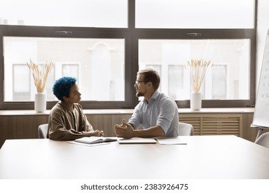 Two positive diverse office friends discussing work business process, teamwork, cooperation, networking in meeting room. Young colleagues talking at large table, collaborating on project - Powered by Shutterstock