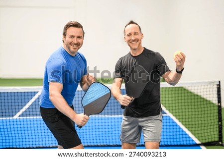 The Two Positive men looking at camera while playing pickleball at court indoor