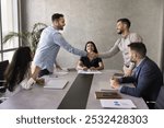 Two positive successful business partners shaking hands over large table. Team of stake holders, project managers, investors ending negotiation meeting with handshake, smiling, laughing