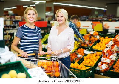 Two positive woman choosing seasonal fruits in grocery section of supermarket