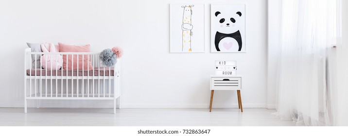 Two posters of painted animals hanging on the white wall in baby room with small cupboard