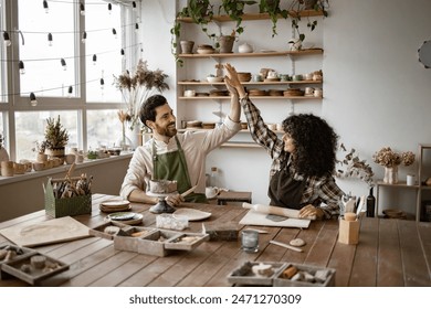 Two pottery artists celebrating with a high five, working together in a creative studio environment. Surrounded by clay, tools, and pottery pieces. - Powered by Shutterstock