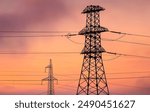 Two power line towers stand tall against a vibrant, orange and purple sunset sky. Power lines at sunset