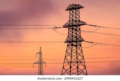 Two power line towers stand tall against a vibrant, orange and purple sunset sky. Power lines at sunset - Powered by Shutterstock