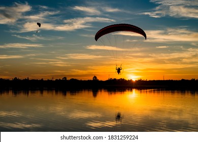 Two powered paragliders flying over the lake during sunrise. Paramotor pilot with reflection in the water