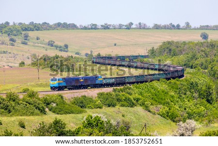 Two powerful diesel locomotives TE33AS pull a very long, heavy train of freight wagons along a winding single-track railway line. Summer shot. Large zoom. Ukrainian railways.