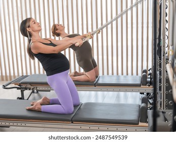 Two pregnant women do Pilates exercises on a reformer. Yoga class for pregnant women.  - Powered by Shutterstock