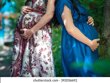 
two pregnant women holding hands on the tummy 