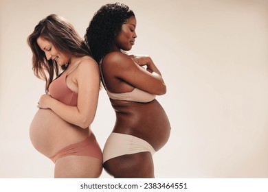 Two pregnant women stand together in a studio, wearing underwear and showing off their changing bodies. Expecting moms proudly embracing the journey of pregnancy and motherhood. - Powered by Shutterstock