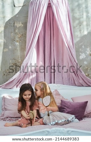 Two preschool girls blonde and brunette are sitting on the bed and playing with the mirror. Vintage interior style.