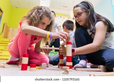 Two pre-school girls playing together with wooden toy blocks on the floor during playtime supervised by a careful young kindergarten teacher - Powered by Shutterstock