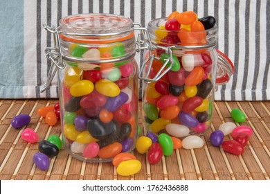 Two Preserving Jars Of Colorful Jelly Beans, One Open, One Closed, On A Bamboo Mat