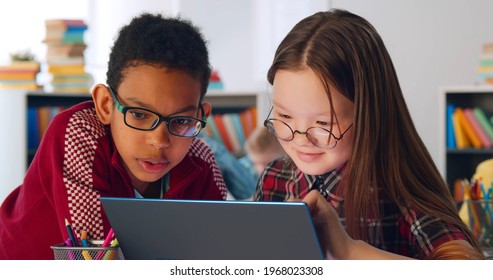 Two preteen diverse students using laptop in classroom. Portrait of asian and african schoolchildren studying on computer together sitting at desk in school class - Powered by Shutterstock