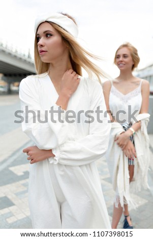 Two pretty beautiful woman  fashion models wear white silk dresses summer collection pose natural beauty storm weather water sea stone beach rock cloudy 