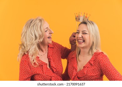 Two Pretty Blonde Caucasian Joyful Women Having Fun Togheter, Laughing And Holding A Fake Crown. Studio Shot. High Quality Photo