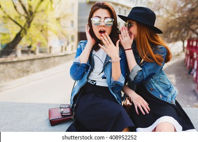 Two  pretty cuter teenagers  shares secrets, gossip. Surprise face, emotions,  Best friends wearing stylish outfit, black hat, sunglasses, dress. Bright spring  colors. 